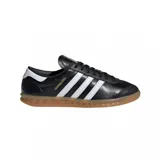 Championes adidas modelo Hamburg, de diseño clásico con exterior de cuero negro, las icónicas tres tiras laterales en blanco y suela de goma color caramelo. Incluye el nombre del modelo en letras doradas en el lateral.