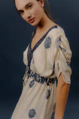 Vestido largo beige con estampado paisley en color azul marino, escote en V profundo con detalle bordado, mangas cortas amplias, cordón ajustable en la cintura con borlas y volados en el ruedo.