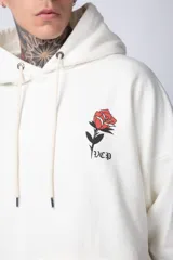 Buzo tipo canguro de corte oversize, color blanco, con capucha y cordones ajustables. Presenta un pequeño estampado de una rosa roja en el pecho y un bolsillo frontal tipo canguro.