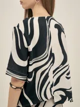 Top de escote redondo y manga corta, con estampado abstracto en blanco y negro. Presenta un corte asimétrico en la espalda y está confeccionado en lino viscosa.