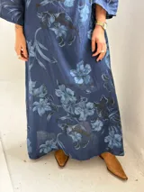 Vestido largo de lino azul marino con estampado floral en tonos más claros, de corte amplio, con cuello tipo cowl y mangas largas.