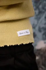 Polera de tejido de punto fino color blanco, con cuello alto, mangas largas y terminaciones con detalle de ondas en puños, cuello y ruedo.