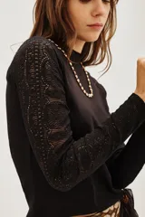 Polera negra de manga larga con diseño combinado, presentando un cuerpo de tejido liso y mangas de encaje con textura. Posee cuello alto y un ajuste entallado al cuerpo.