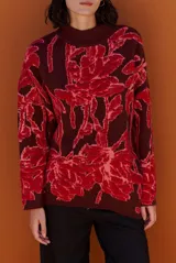 Buzo de tejido de punto con diseño floral en contraste, cuello redondo y mangas largas. Presenta una textura suave y un corte holgado.