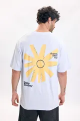 Remera celeste de manga corta y corte oversize, con estampa grande en la espalda que incluye un diseño abstracto de sol amarillo y textos negros.