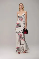 Vestido largo de satén con estampado tipográfico en tonos negro y rojo sobre fondo blanco. Presenta escote degagê, breteles finos y una caída fluida que estiliza la figura.