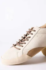 Championes urbanos de gamuza color marrón, con suela de goma en tono crema y cordones jaspeados. Presenta un refuerzo en la puntera y un detalle en cuero beige en el talón.