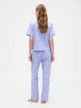Pijama de dos piezas confeccionado en popelina, compuesto por una camisa de manga corta con cuello solapa y cierre frontal de botones, y un pantalón largo de corte recto con cintura elástica. Presenta un estampado integral de cerezas sobre fondo rosado.