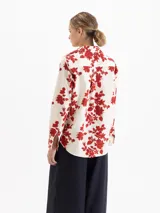 Camisa de poplin de algodón con estampado floral y de fresas en color rojo sobre base crema. Presenta cuello camisero, cierre frontal con botones y mangas largas con puños abotonados.