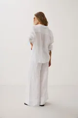 Camisa oversize blanca de manga larga con cuello camisero, bolsillo frontal en el pecho y cierre de botones.
