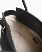 Cartera tipo tote color negro, con diseño estructurado, doble asa corta y correa larga ajustable y desmontable. Cuenta con detalles metálicos dorados y placa frontal con el logo de la marca.