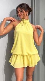 Vestido corto amarillo de gasa, con escote halter alto y falda con volados en el borde inferior.