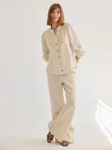 Camisa de corte recto y manga larga, confeccionada en algodón blanco. Presenta un canesú superior con bordado inglés floral y detalle de placa metálica con logo en la espalda.