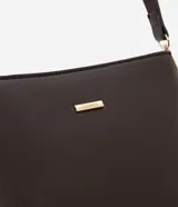 Cartera tipo hobo de tamaño pequeño, confeccionada en material sintético color marrón oscuro con acabado liso. Presenta una correa ajustable, cierre principal con cremallera y detalles metálicos dorados, incluyendo una placa con el logo de la marca en el frente.