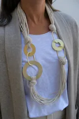 Collar largo de diseño artesanal compuesto por múltiples cordones de algodón en color crudo, entrelazados con aros y eslabones metálicos en tono dorado mate.