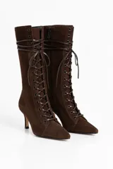 Botas de caña media en cuero gamuzado color chocolate, con diseño acordonado frontal estilo corset y cierre lateral. Presentan punta fina y taco alto fino.
