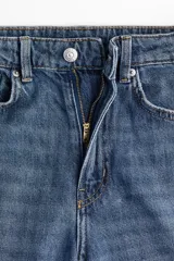 Jean de tiro alto confeccionado en denim de algodón rígido, con diseño de cinco bolsillos, perneras amplias y corte holgado. Presenta un lavado azul medio y detalle de dobladillo deshilachado.