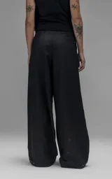 Pantalón sastrero de corte oversize, color negro, con pinzas frontales que forman tablones profundos, cintura ancha, presillas robustas y bolsillos laterales y traseros tipo ojal.