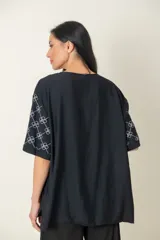 Blusa negra de viscosa con estampado de flores blancas en las mangas, corte holgado, cuello redondo y botones frontales.