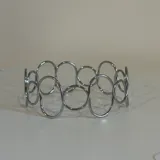 Brazalete rígido plateado formado por círculos unidos entre sí.