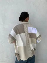 Camisa tipo chaqueta con diseño a rayas horizontales en tonos beige, blanco y marrón, con cuello camisero, cierre frontal con botones, mangas largas y bolsillos de cuero en el pecho.