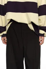 Pantalón tobillero de corte campana color negro, confeccionado en mezcla de algodón y viscosa. Presenta cierre frontal con botón, tiro medio, bolsillos diagonales, cinturilla elástica y vuelta en el bajo de la pierna.