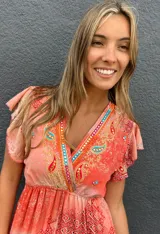 Vestido largo anaranjado con estampado estilo paisley y geométrico, escote en V con bordados multicolor, mangas cortas con volados, cordón ajustable en la cintura con borlas turquesas y falda escalonada.