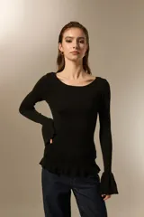 Remera de punto al cuerpo con cuello bote y mangas largas terminadas en volados acampanados. Presenta un ruedo con detalle de volados.