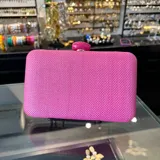 Clutch rectangular rígido de rafia sintética color fucsia, con cierre a tono y asa desmontable de cadena dorada para llevar al hombro.