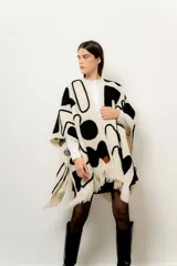 Ruana tejida en lana con diseño de formas abstractas en color negro sobre fondo crudo, con terminación de flecos en el ruedo.