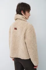Chaqueta tipo gamulán de color marrón, con solapas amplias forradas en corderito sintético oscuro. Presenta un diseño cruzado con botones frontales y mangas largas, ideal para un estilo invernal.