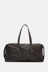 Bolso de hombro con diseño alargado confeccionado en nylon de color marrón oscuro. Presenta doble asa de mano en material a contraste, cierre superior con cremallera metálica y botones laterales decorativos.