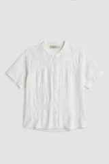 Camisa de manga corta color blanco con cuello mao y cierre frontal de botones. Presenta detalles bordados tono sobre tono en el canesú y diseño de corte recto.