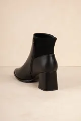 Botas de caña baja color negro, de símil cuero con punta redonda, cierre lateral, taco cuadrado y recorte en gamuza en la parte trasera.