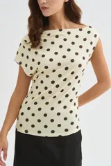 Top de poliéster negro con estampado de lunares blancos, diseño al cuerpo y cuello asimétrico de manga corta.