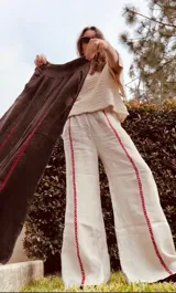 Pantalon de lino tiro alto, corte wide leg y diseño holgado, con detalles de costuras bordadas en contraste a lo largo de las piernas.