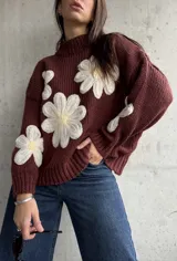 Sweater de punto color chocolate con diseño de flores grandes en relieve en color crema y centro amarillo. Presenta cuello alto, mangas largas y corte holgado.