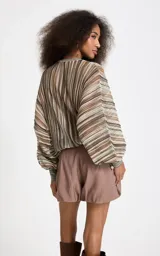 Blusa de punto con rayas verticales en tonos marrón, beige, verde y blanco, corte amplio, escote redondo y mangas largas anchas con puños ajustados.