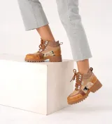 Borcego de cuero color marrón con paneles de tela texturizada y estampado animal print. Tiene cordones marrones, herrajes metálicos y suela de goma con plataforma.