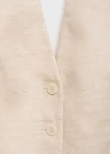 Chaleco sastrero de lino color beige, con cuello halter pronunciado y cierre frontal de cuatro botones. Presenta bolsillos ribeteados simulados en el frente y dobladillo en punta.