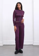 Conjunto de pantalón y top color morado con costuras celestes a la vista. El pantalón es de corte ancho y el top es de manga larga con cuello alto.