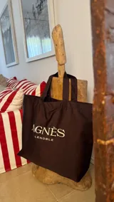 Tote bag de gran tamaño, color marrón, con doble asa larga para hombro y estampado con el logo de la marca Agnès Lenoble en el frente.