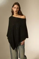 Poncho negro de tejido de punto con diseño asimétrico y detalle de pequeñas aplicaciones brillantes distribuidas por toda la superficie. Presenta un borde acanalado en el ruedo.