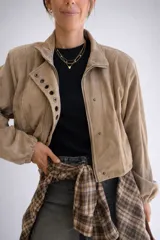 Chaqueta corta de efecto gamuza con cierre frontal y botones. Presenta mangas tipo globo con puños elásticos y detalle de aros metálicos decorativos en la solapa. Cuenta con ajuste lateral en la cintura y forro interior.