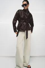 Chaqueta de Zara Woman Collection confeccionada en tejido efecto piel con textura granulada. Presenta cuello solapa, manga larga y cierre frontal con cinturón ajustable anudado a la cintura. Incluye forro interior.