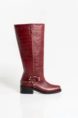Botas de caña alta en cuero con textura de cocodrilo, color bordó. Presentan un diseño de punta cuadrada, taco bajo y una correa decorativa con argolla metálica y remaches en la zona del tobillo.