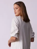 Blusa de color blanco con torso de modal y mangas cortas con detalle de bordado calado. Presenta cuello redondo con apertura central abotonada.