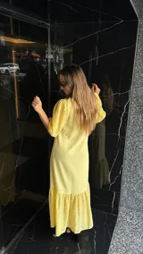Vestido largo color amarillo pálido, con escote en V, mangas cortas abullonadas con detalle de calado y ruedo con volantes y calado.