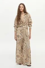 Pantalón de pierna ancha y tiro medio, confeccionado en mezcla de lino y viscosa, con cintura elástica y cordón ajustable. Presenta un estampado artesanal en tonos beige y marrón.