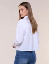 Camisa blanca estilo crop de la marca Zac & Rachel, confeccionada en mezcla de algodón. Presenta cuello con solapa, cierre frontal con botones, manga larga con puño ancho abotonado y diseño de corte corto.
